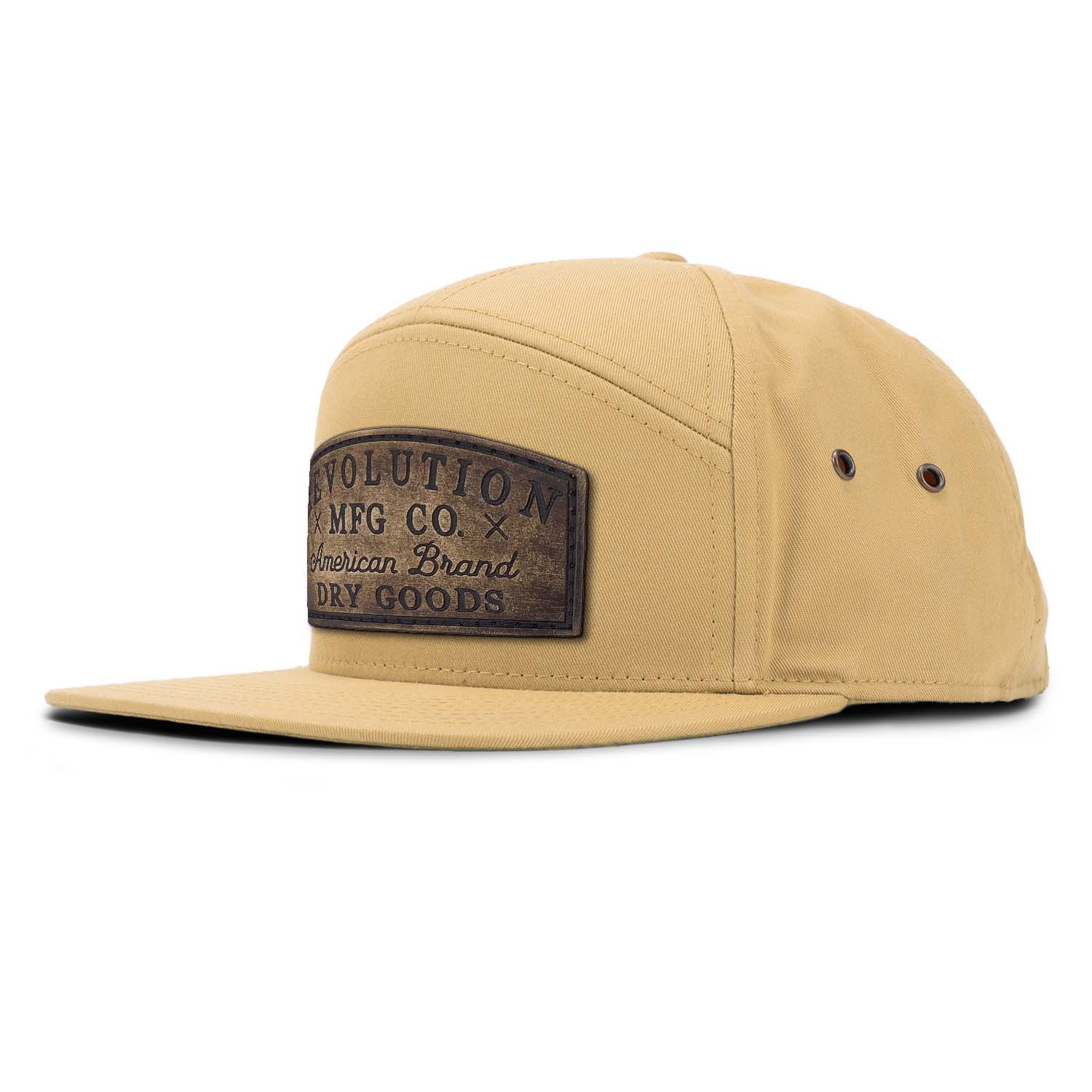 A biscuit tan 7 panel style hat featuring an adjustable leather strapback with brass clasp closure and brass eyelets with our full grain leather vintage Dry Goods patch on the seamless front panel