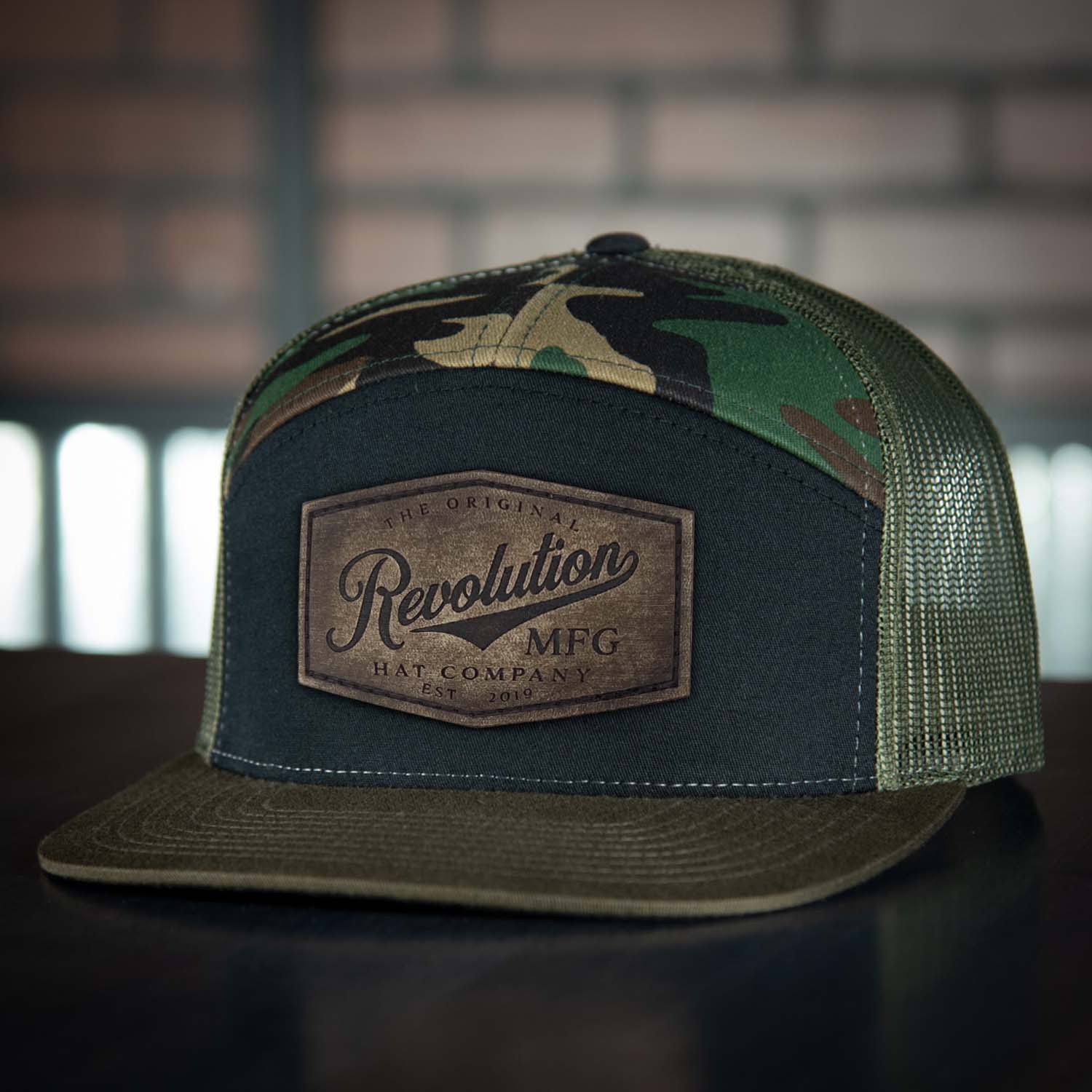 Revolution Hat Co Vintage full grain leather patch stitched on a black, woodland, and loden 7 panel flat bill trucker hat