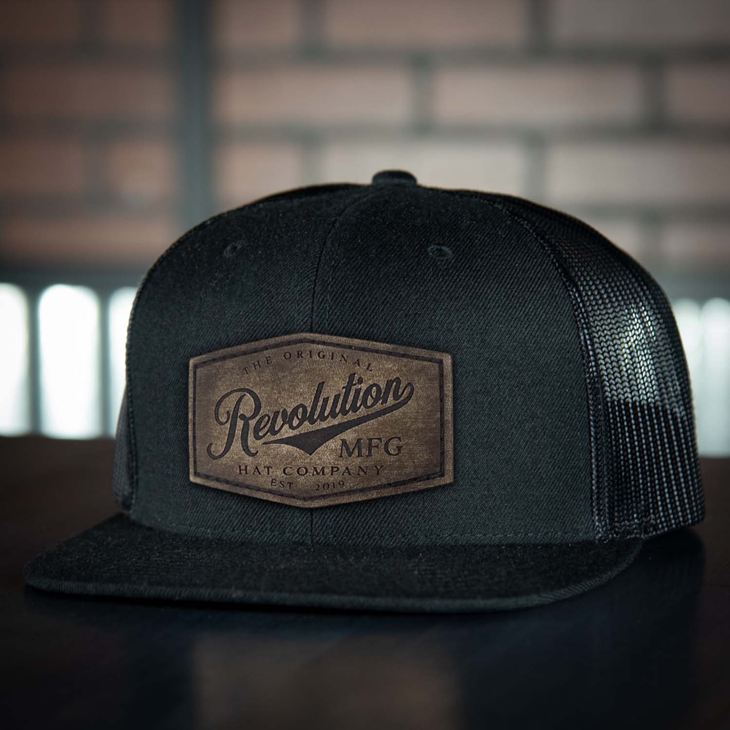 Revolution Hat Co Vintage full grain leather patch stitched on an all black 7 panel flat bill trucker hat