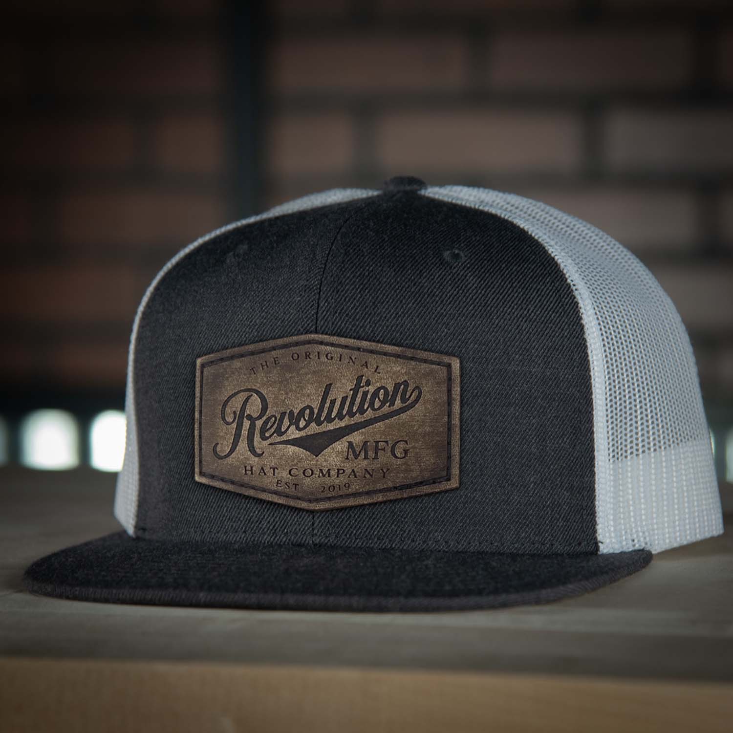 Revolution Hat Co Vintage full grain leather patch stitched on a charcoal gray and white 7 panel flat bill trucker hat