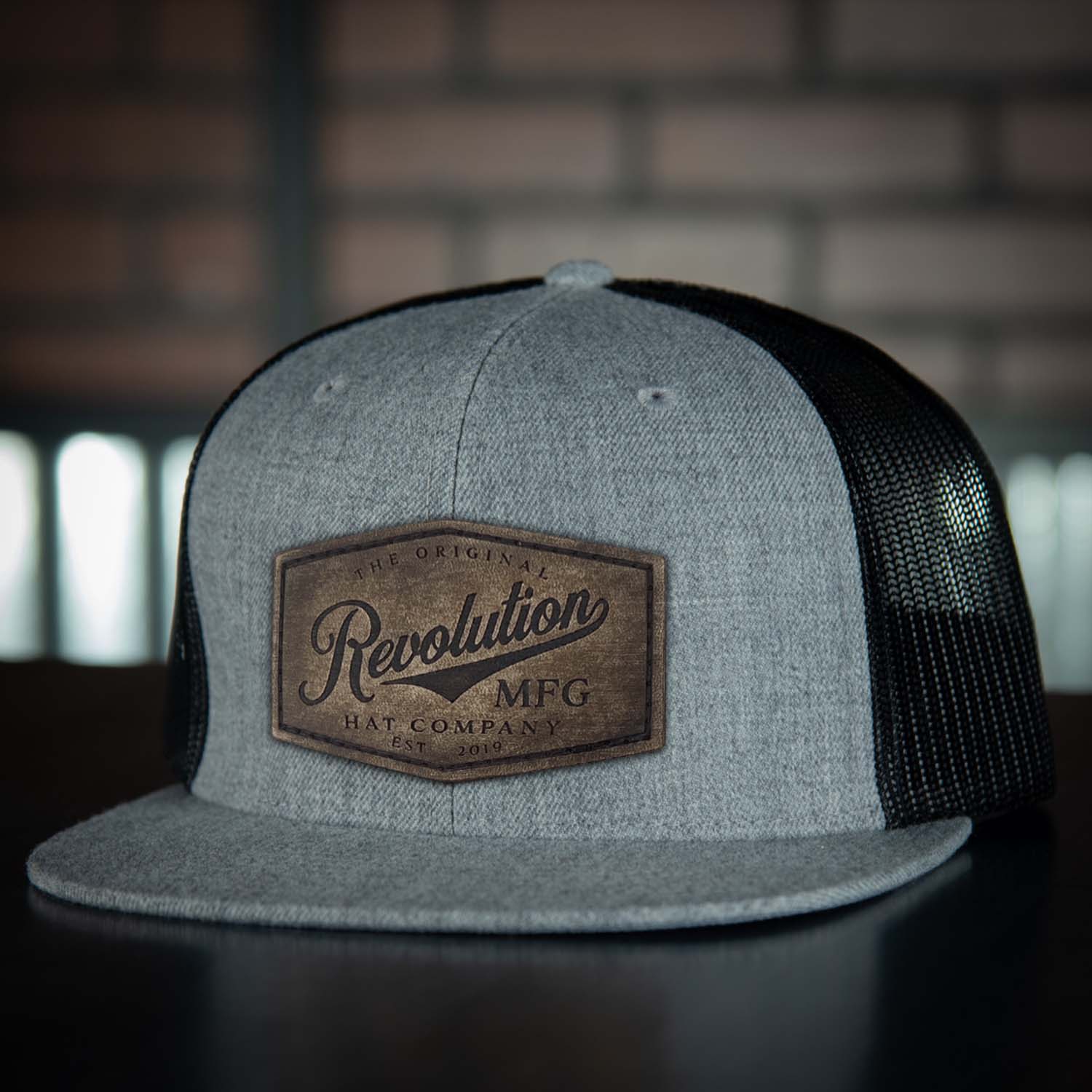 Revolution Hat Co Vintage full grain leather patch stitched on a heather gray and black 7 panel flat bill trucker hat