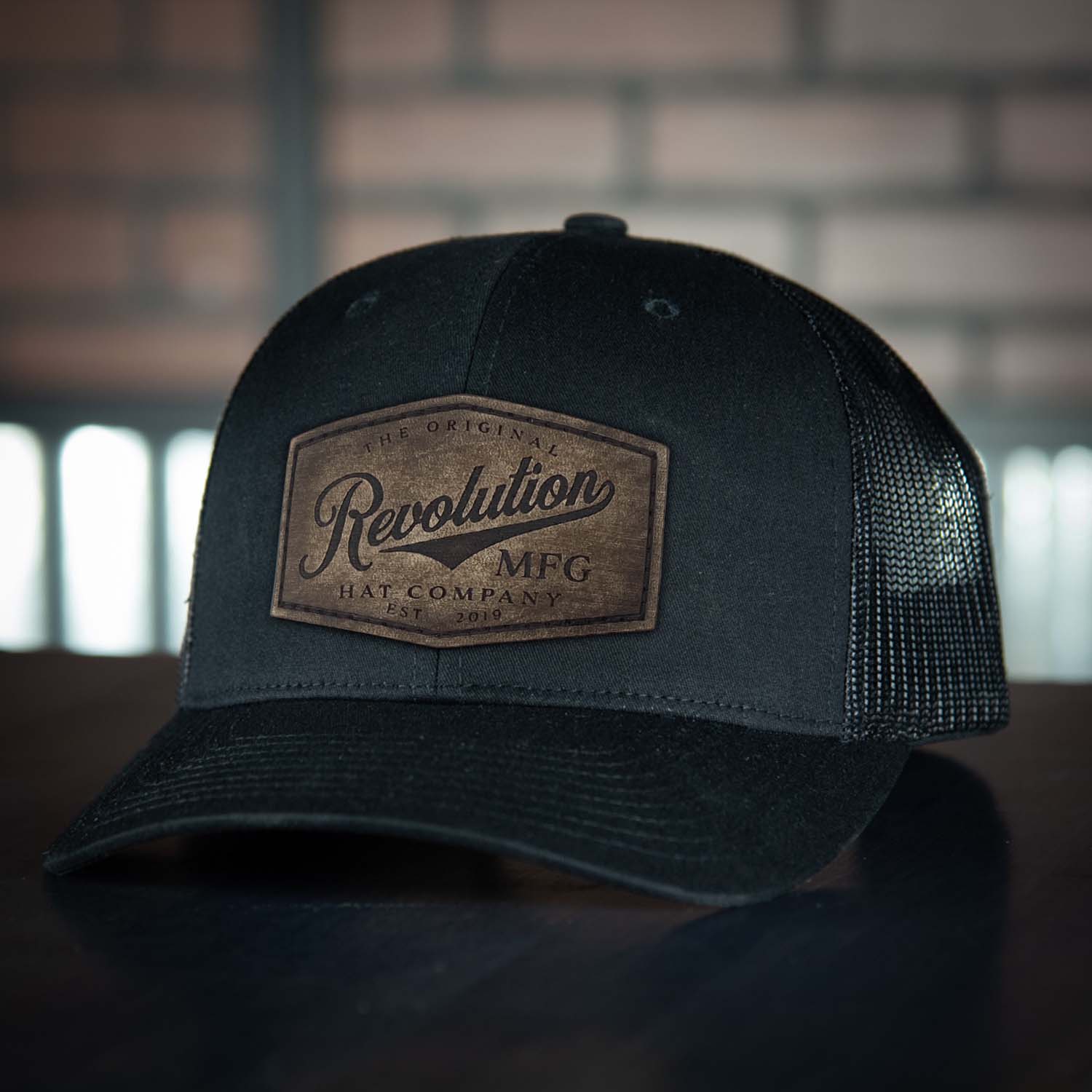 Revolution Hat Co full grain leather patch in a vintage finish on a black with black mesh classic trucker hat