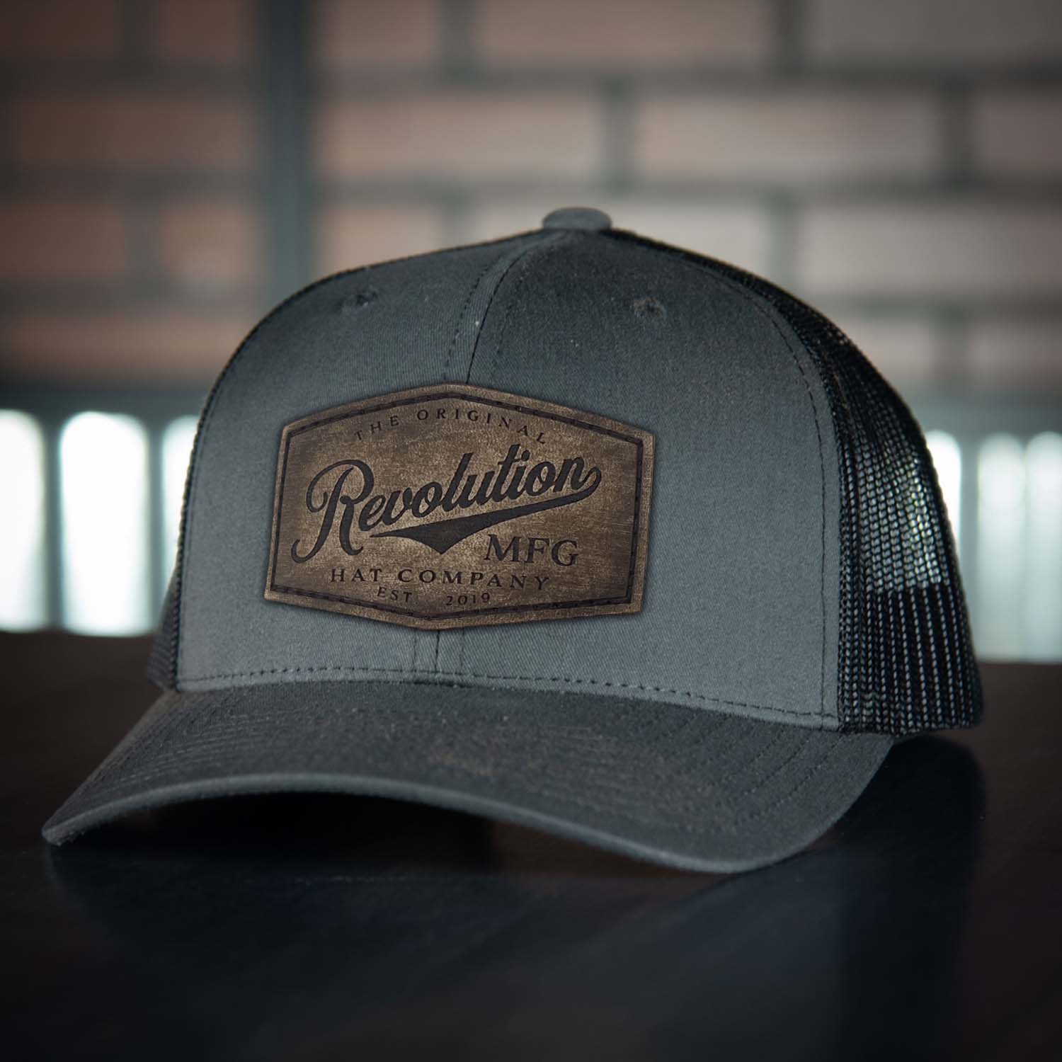 Revolution Hat Co full grain leather patch in a vintage finish on a charcoal with black mesh classic trucker hat